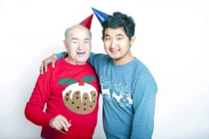 Image of a young Asian man and an older Caucasian man in Xmas sweaters