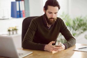 Man frowning at a text message on his phone. Sitting at desk.